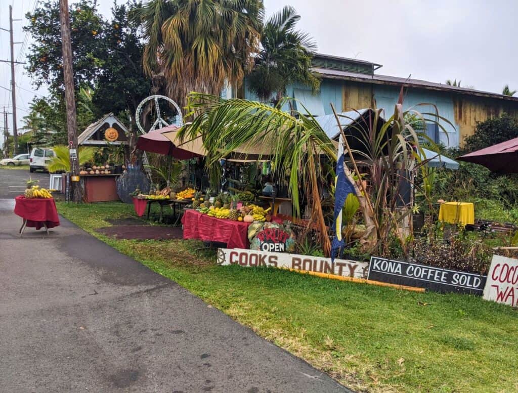 cooks bounty fruit stand loaded with tropical fruit and hand painted signs advertising what is is available: kona coffee, coconut water, fruit.