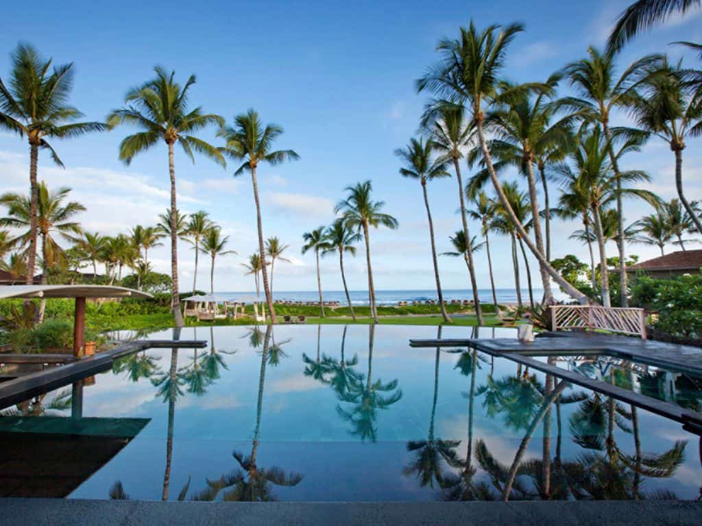 Four Seasons Hualalai infinity pool surrounded by palm trees and ocean in the background