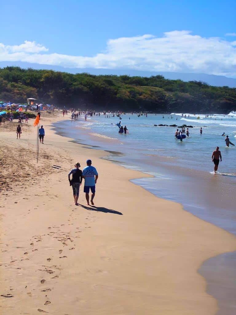 A sandy beach on the Big Island filled with people swimming and walking along the shoreline under a bright blue sky. Relaxing at popular beaches like this is a classic way to unwind during a big island itinerary 4 days trip.