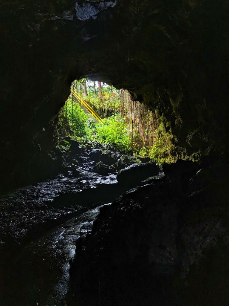 View from inside a dark lava tube looking out toward lush green vegetation and sunlight streaming through the cave opening on the Big Island. Exploring lava tubes like this adds a unique adventure to a big island itinerary 4 days trip.