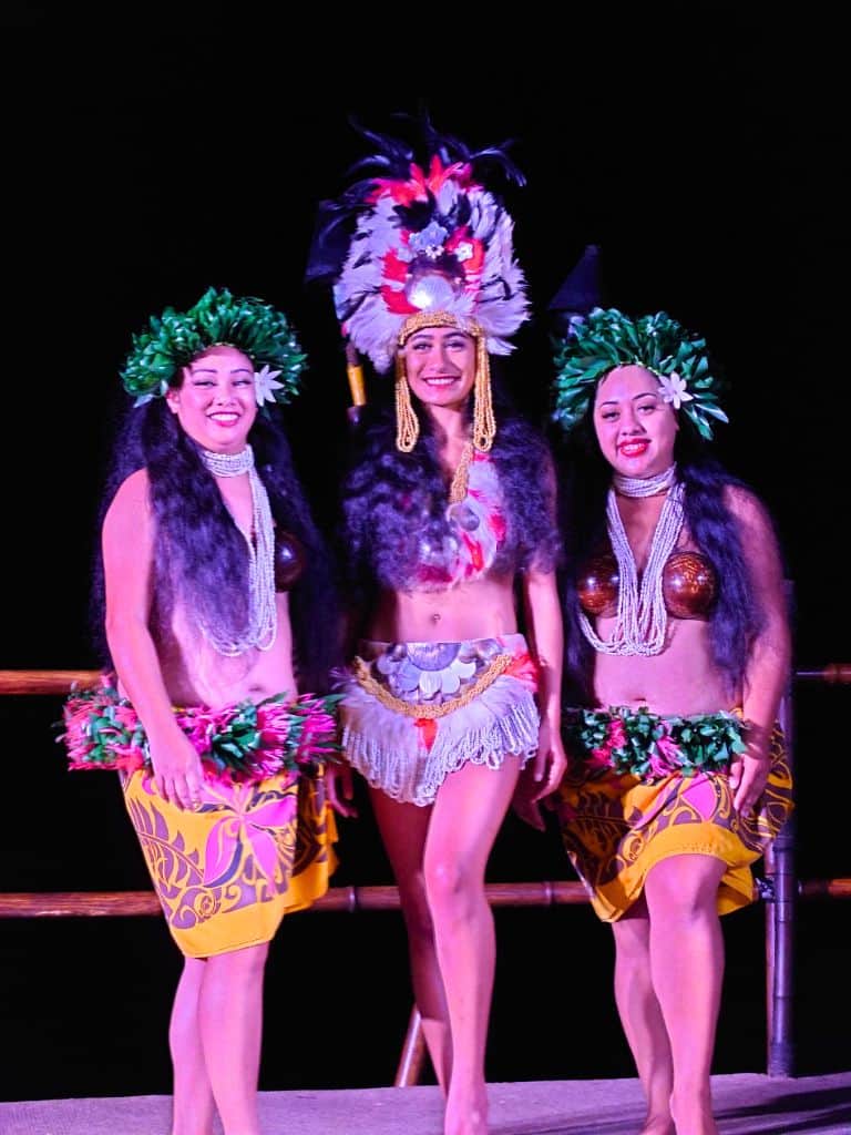 Three performers in traditional Hawaiian attire with leafy headpieces, shell jewelry, and feathered headdresses pose on stage during a cultural show on the Big Island. Attending a luau or cultural performance like this adds an authentic experience to a big island itinerary 4 days trip.