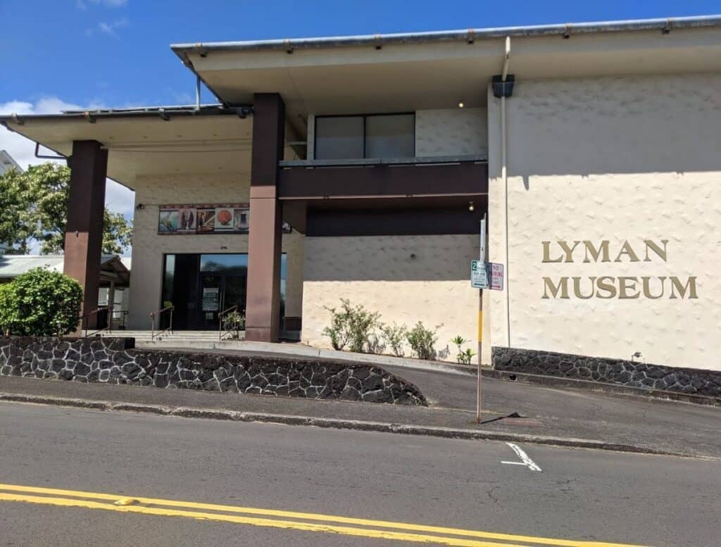 Exterior of the "Lyman Museum" building in Hilo Hawaii with beige walls, dark columns, and a sign reading "Lyman Museum" on the front. Visiting local museums to learn about Hawaiian history and culture is one of the educational things to do in Hilo Hawaii.
