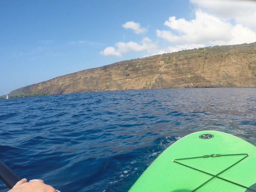 View of the brown cliffs in Kealakekua Bay from my green paddle board on blue water