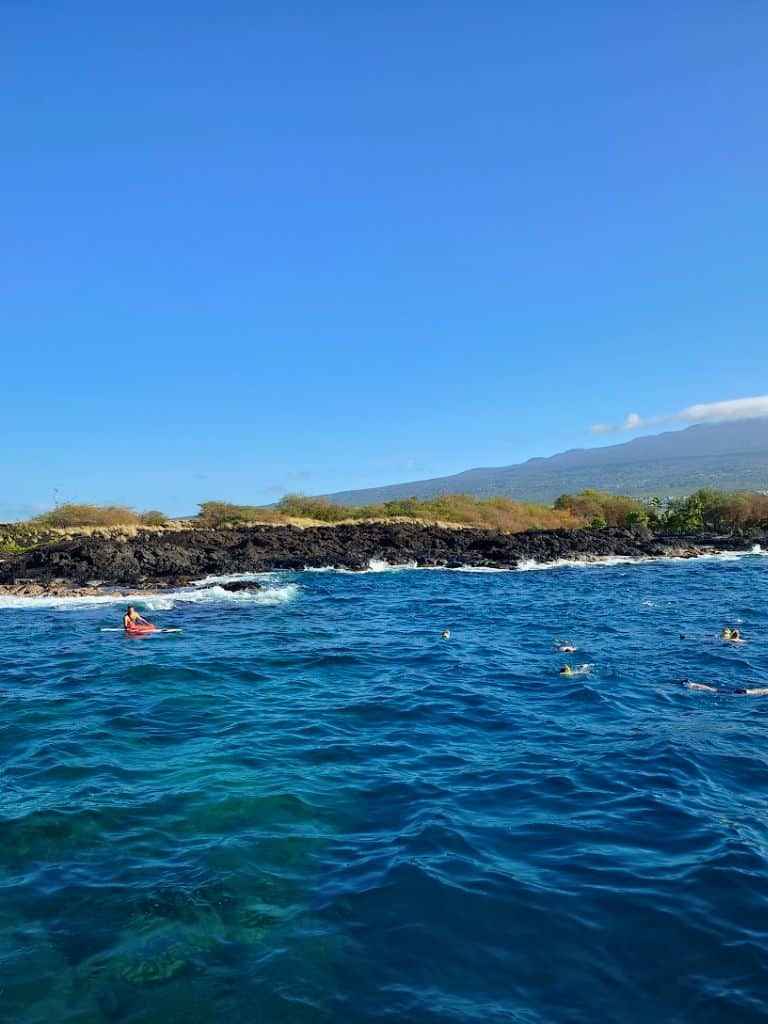 Snorkelers in Pawai Bay with Body Glove crew member keeping watch in blue water along rocky coastline