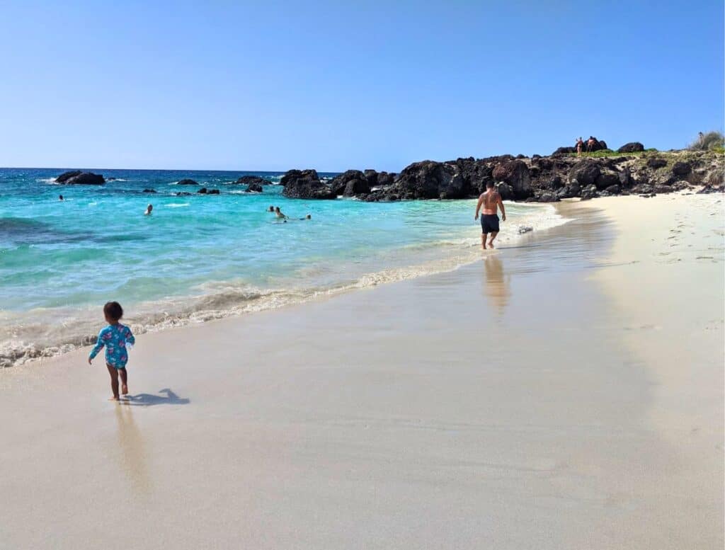 man and child walking on Kua Bay Beach whit sands with blue waters
