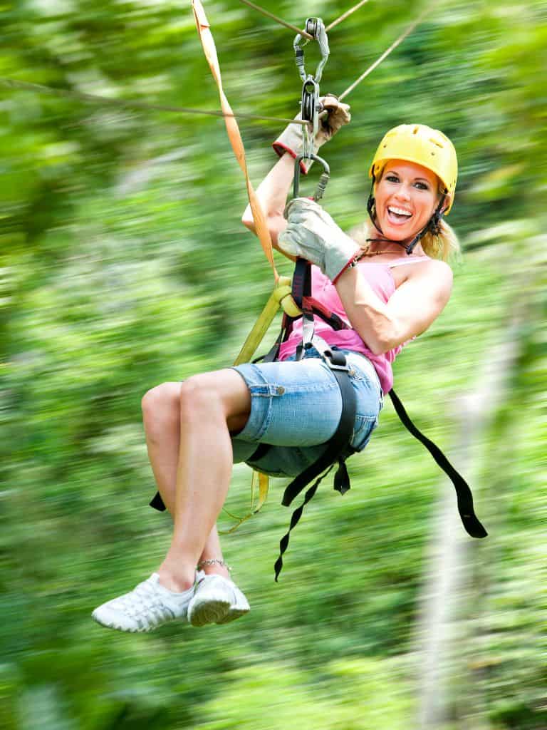 lady happy ziplining with forest blurred in background