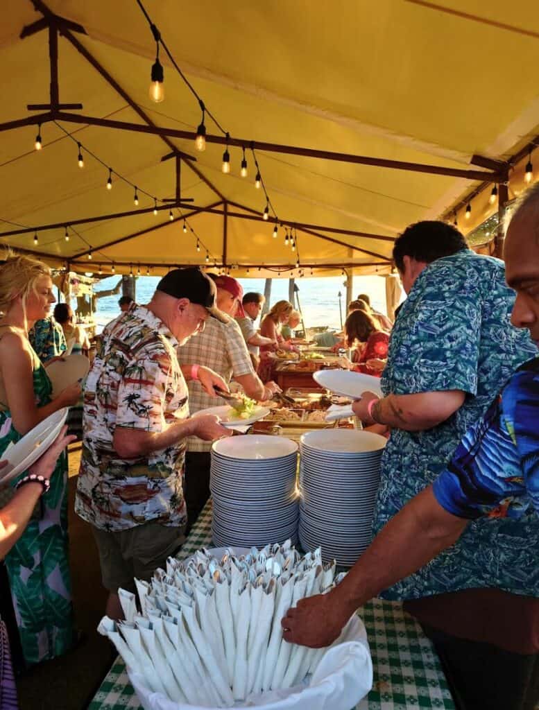 people grabbing silverware and plates at the beginning of the Buffet table under a tent