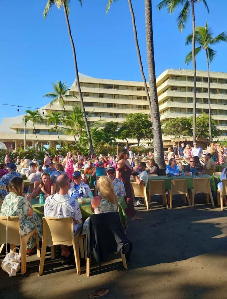 a crowd of Luau guests in general admission seating at tables with royal kona resort in background