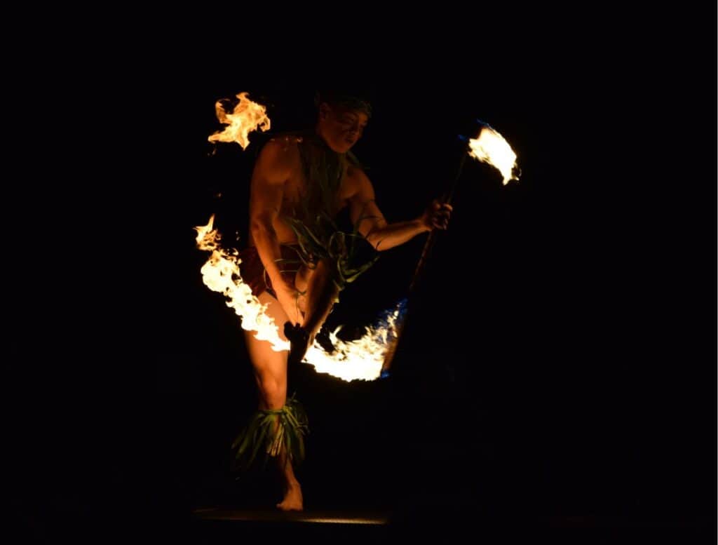 Fire dancer performing at night while spinning flaming torches during a traditional Hawaiian luau show. Watching a fire knife dance performance is one of the most exciting cultural things to do Waikoloa visitors can experience in the evening.