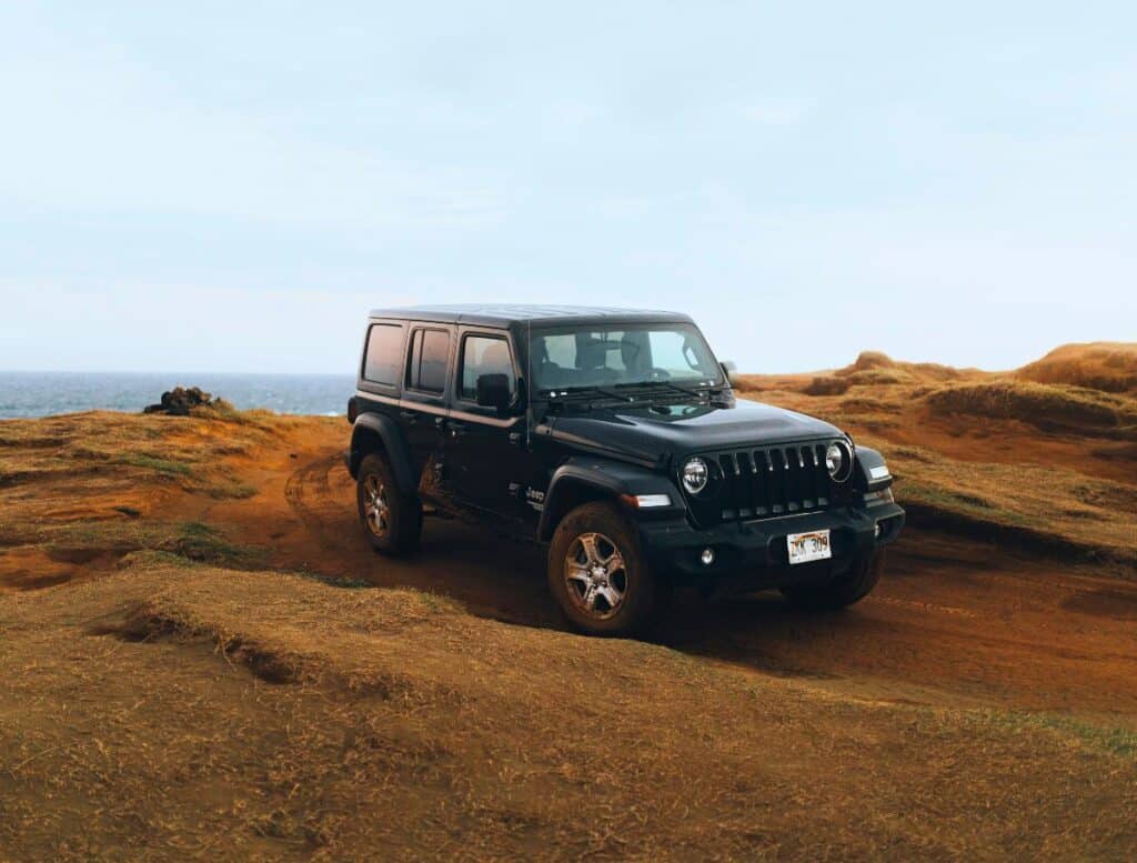 black jeep wrangler driving the red dusty paths to green sand beach