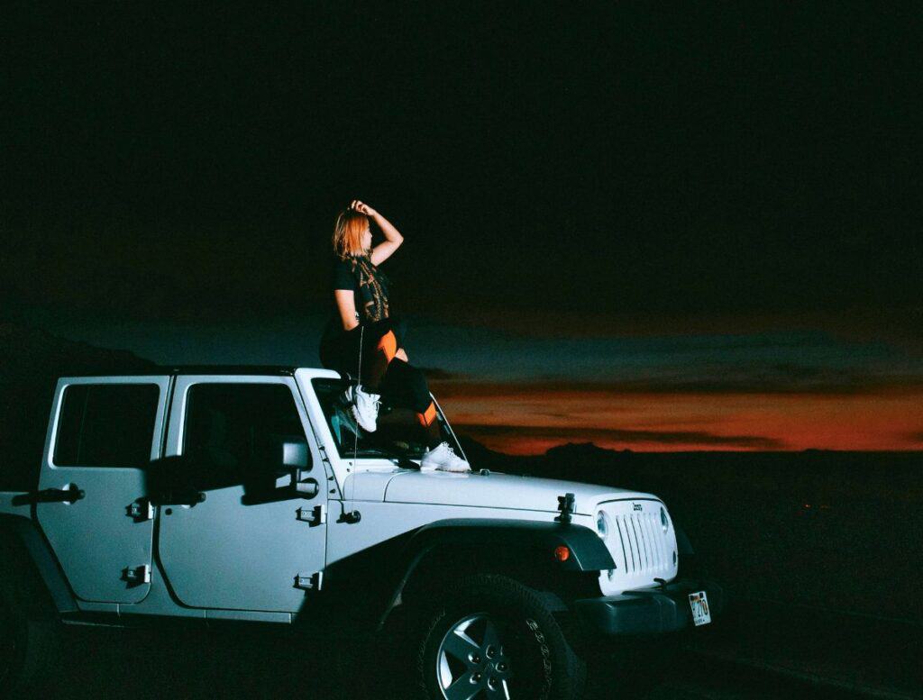 girl sittin on top of white jeep looking at last remnants of sunset