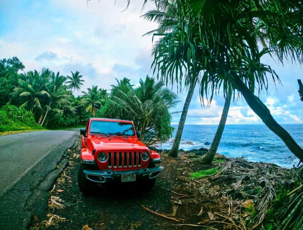 red jeep parked on the side of the road next to the ocean with palm trees surrounding it