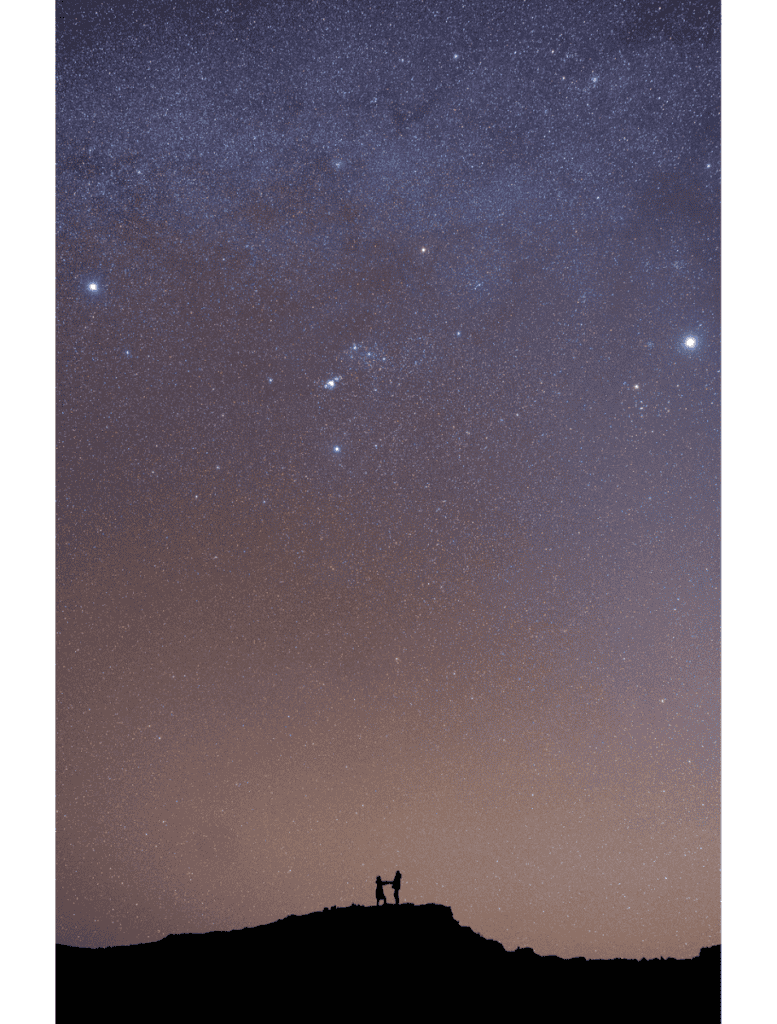 couple standing on a rocky plateau silhouetted against the starry sky background