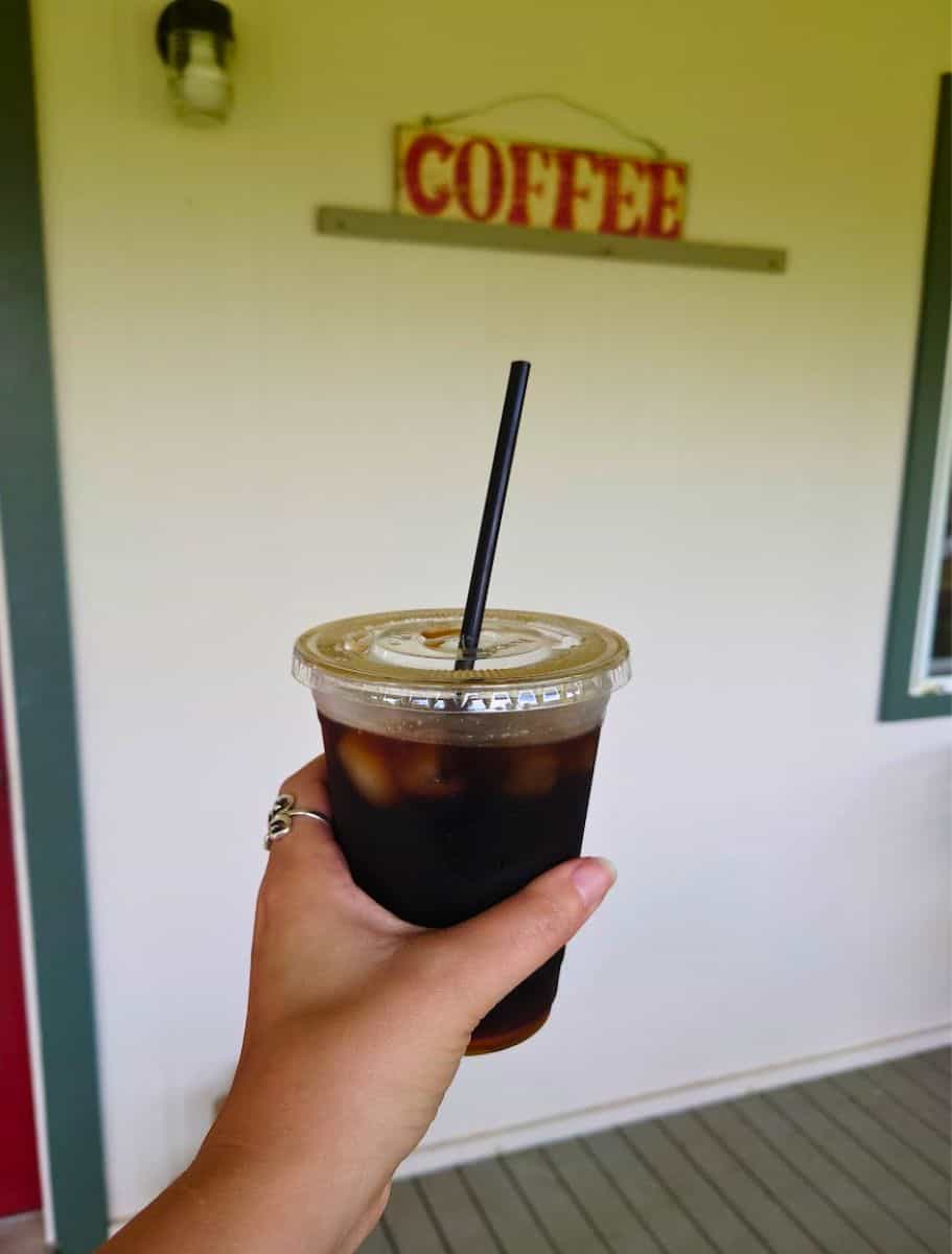 hand holding iced cup of coffee with the sign "coffee" on wall