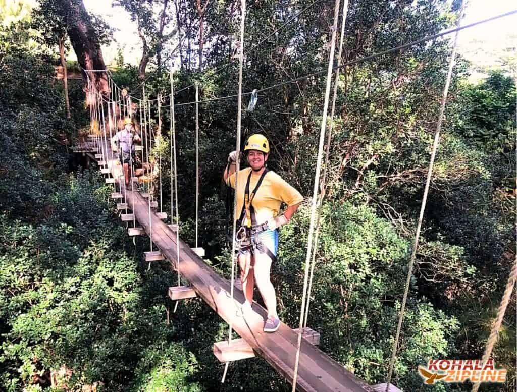 Me posing with hand on hip, safely clipped in on a suspension bridge above forest with person coming up behind me