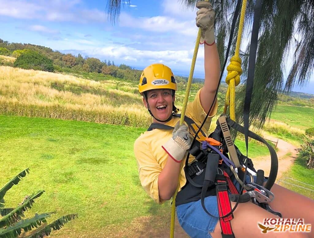 Me rappelling out of the final tree with grass below me and faint view of ocean in the distance