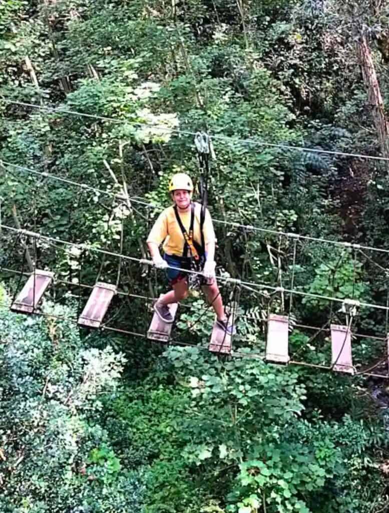 Me facing my fear of heights on one of the suspension bridges clinging to the rope railing and wooden slats spaced far apart below my feet