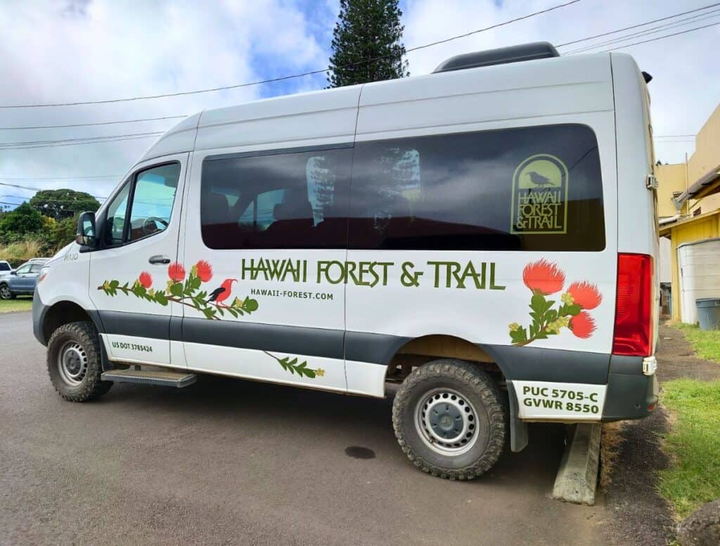 Our van ride to the zipline course; a white van that reads Hawaii Forest & Trail and lehua and i'iwi picture on it