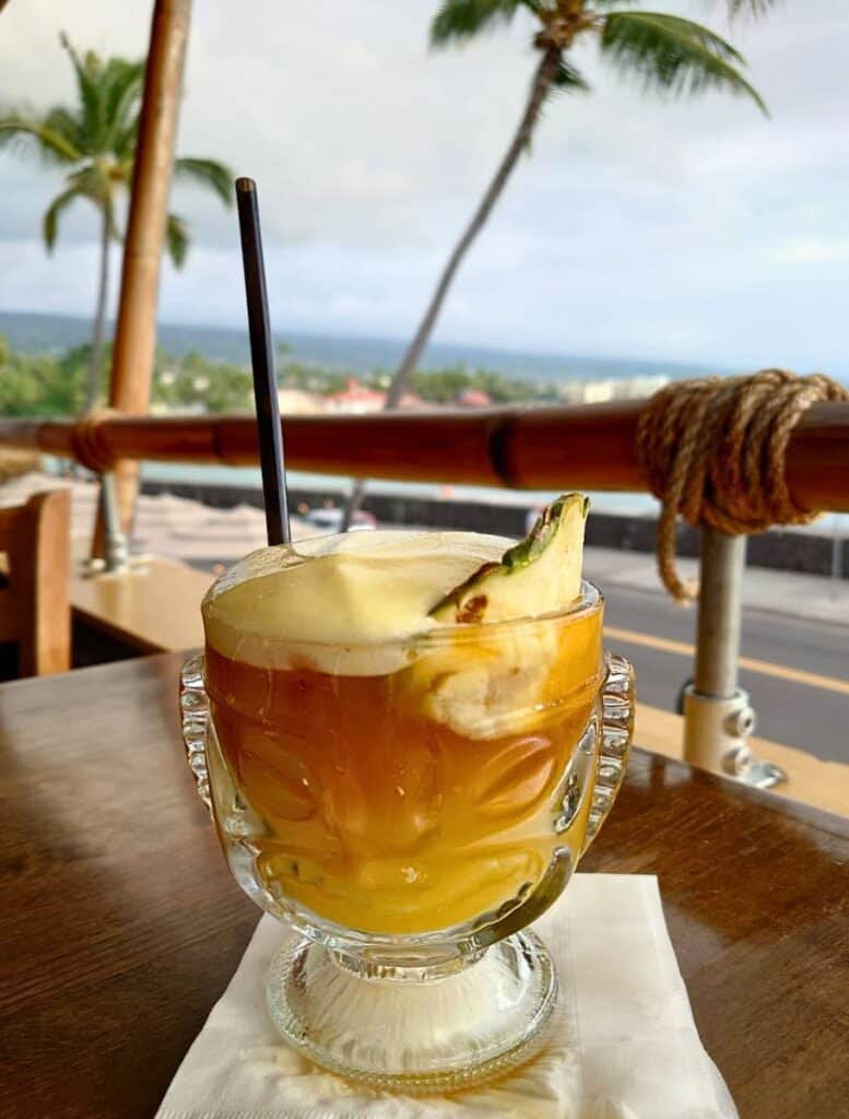 Cheeky Tiki mai tai with lilikoi foam in clear tiki face glass on the second story overlooking ali'i drive