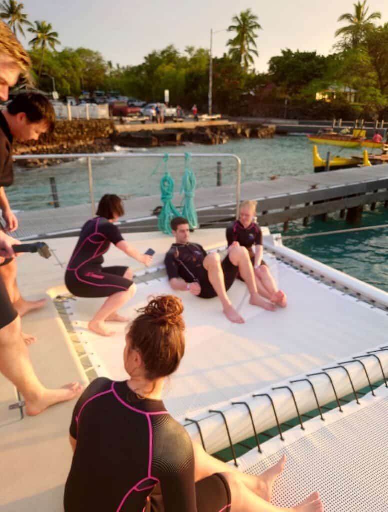 people in wetsuits sitting around the edge of the Overwater net on the back of the catamaran