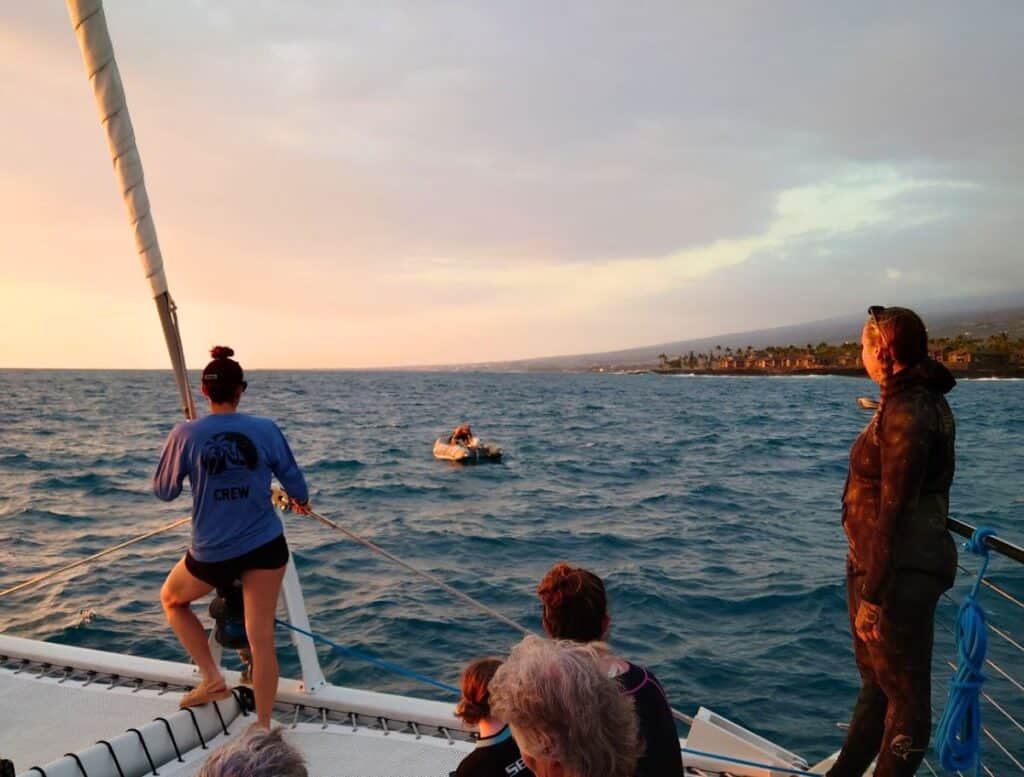 small raft next to our boat with crew member who saved our "parking spot" in the water. crew members looking on from the catamaran