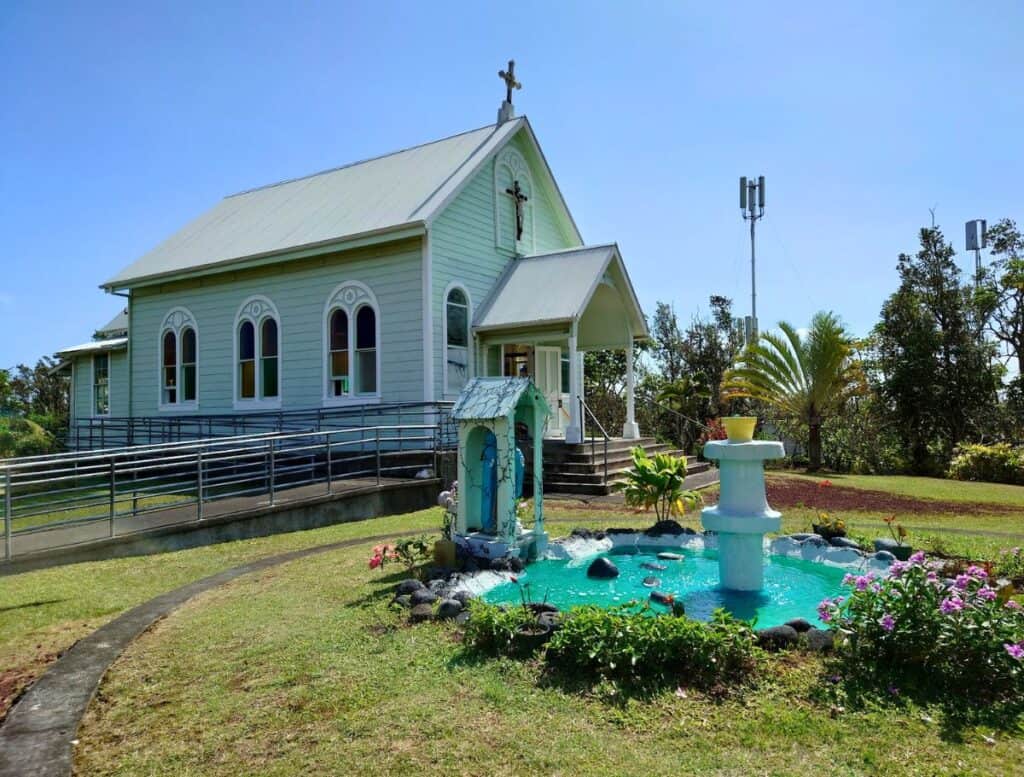 Exterior of the Star of the Sea Painted Church, a quaint sea foam green chapel with a blue pond with fountain and statue in gardenesque surrounding