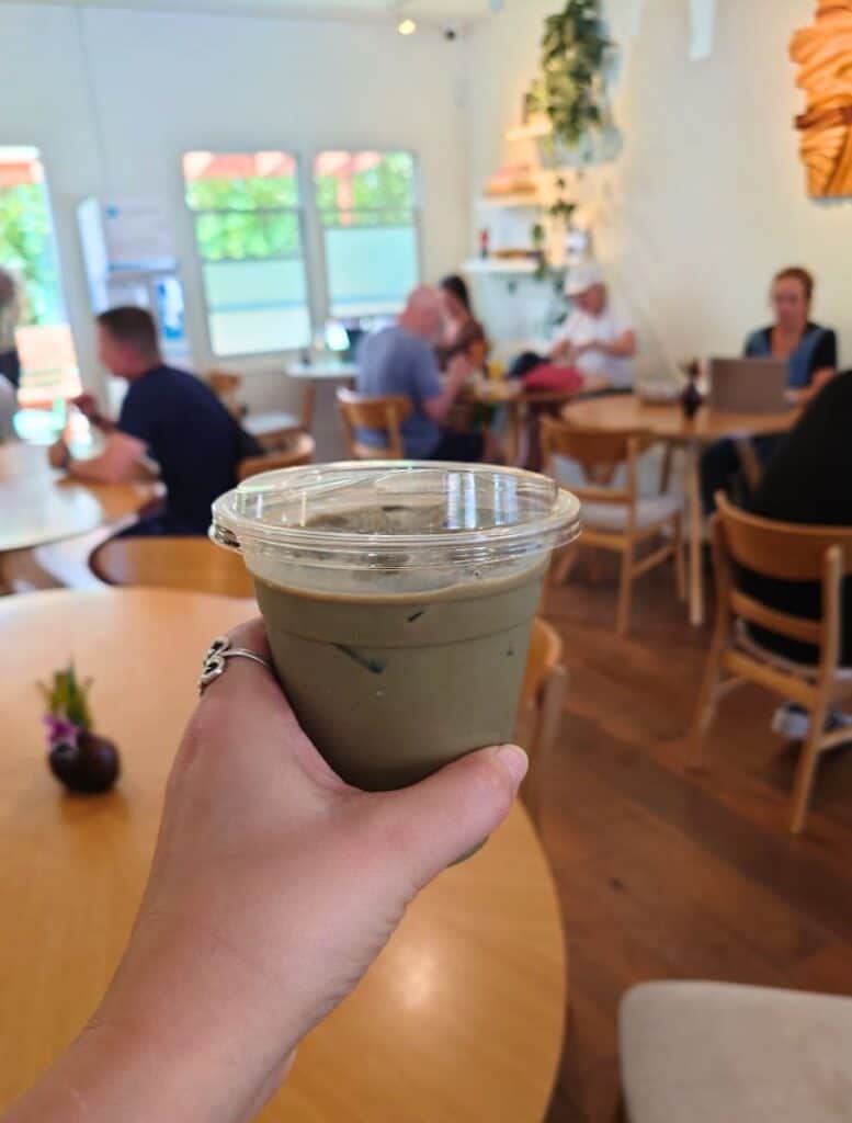 my hand holding an Black Sesame Iced Latte from Surf Camp Coffee