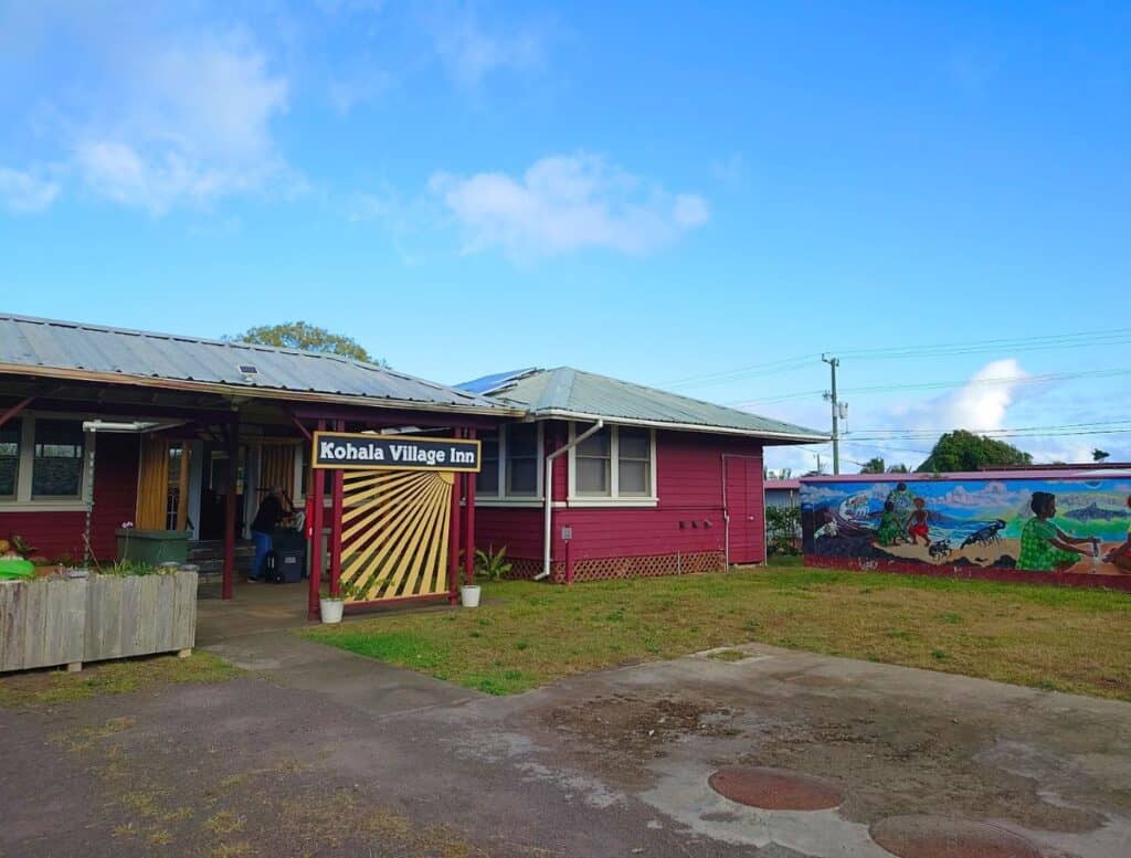Front entrance to Kohala Village Inn with sun ray design wall made of wood and large mural painting on building next door