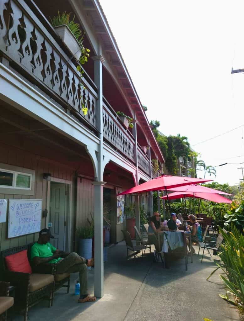 two story My Hawaii Hostel in Kona with people sitting at tables under umbrellas