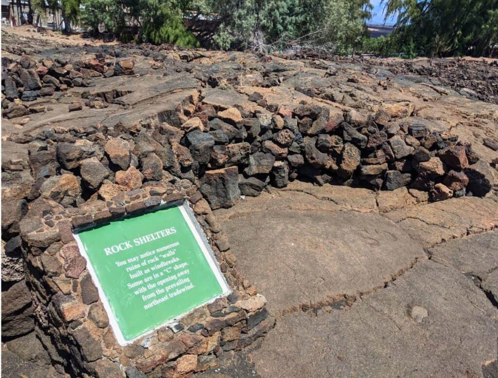 Waikoloa Petroglyph Reserve rock shelter. sign reads: rock shelters. you may notice numerous ruins of rock "walls" built as windbreaks. some are in a "c" shape with the opening away from the prevailing northeast tradewind