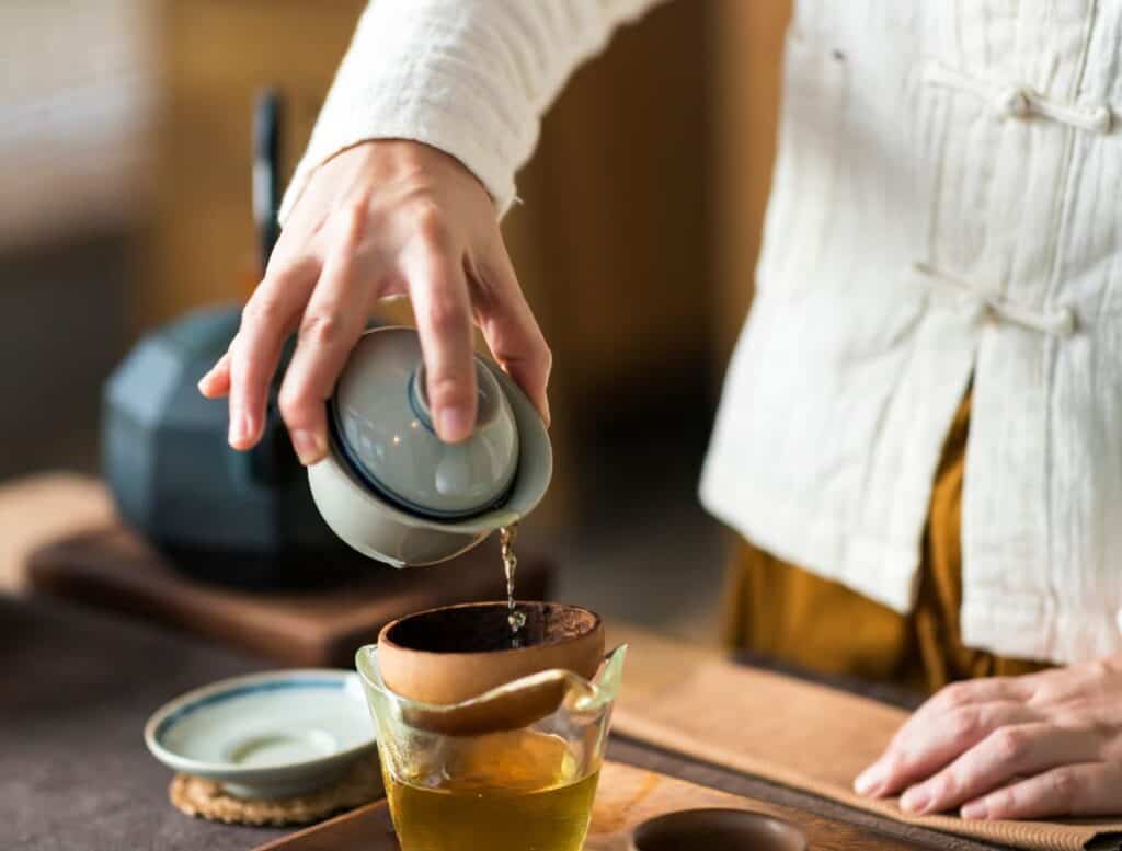 hands pouring tea from pot to cup in tea ceremony