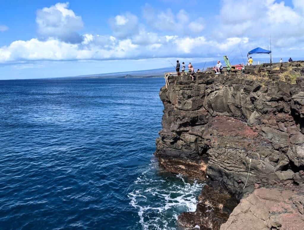People fishing from South Point cliffs. blue water below cliffs. fishing poles everywhere. tent set up.