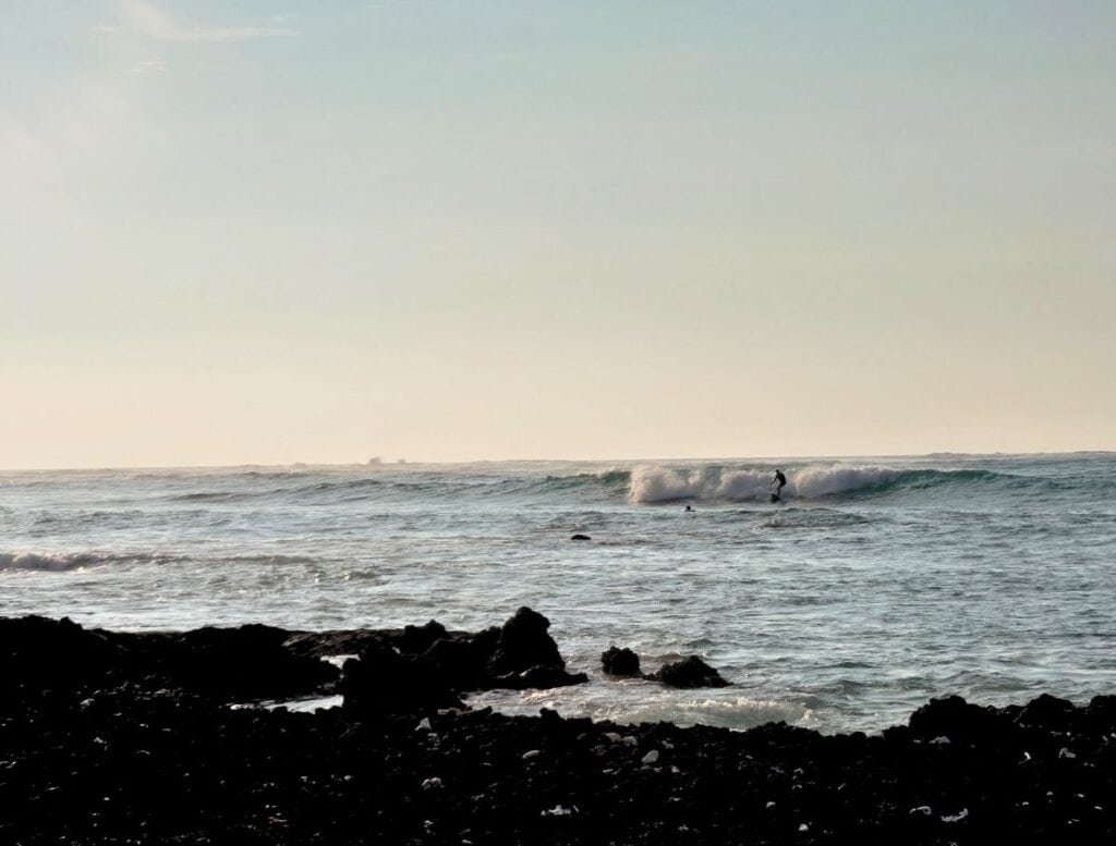 Surfer riding wave off Big Island rocky beach