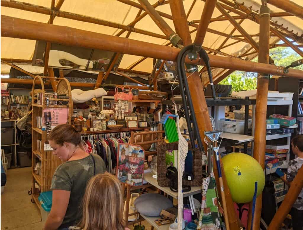 inside Thrift store tent at Waiohinu Transfer Station Reuse Center with rows of clothes, games, and household goods with two shoppers